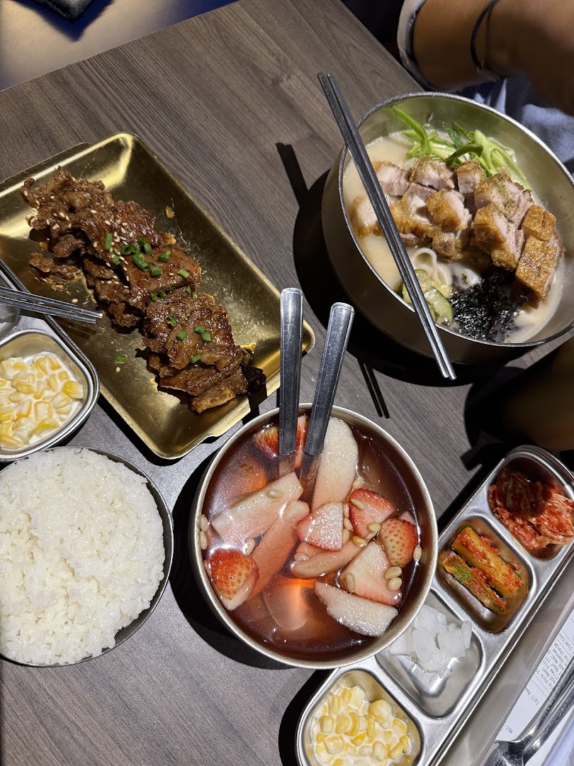 A table laden with delicious Korean dishes including BBQ, noodle soup, rice, and banchan.