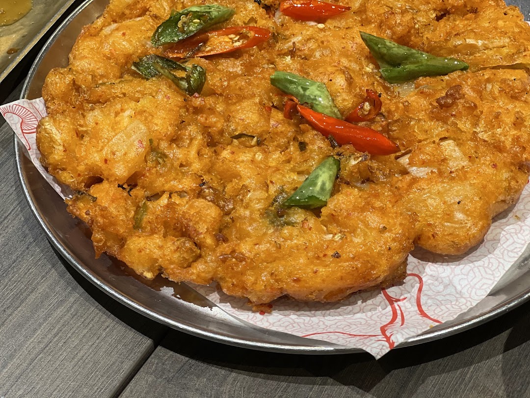 A close-up of a golden-fried dish garnished with red and green chili peppers and herbs on a metal plate.