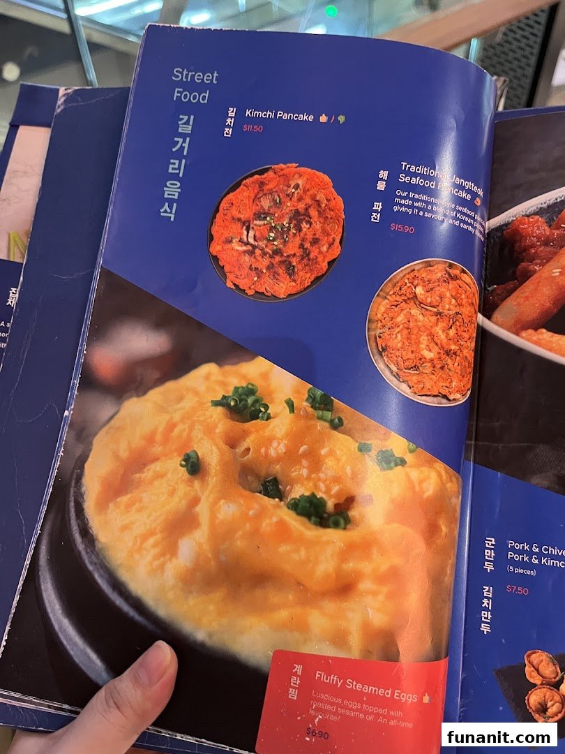 A close-up view of a Korean restaurant menu, featuring street food items like pancakes and steamed eggs.