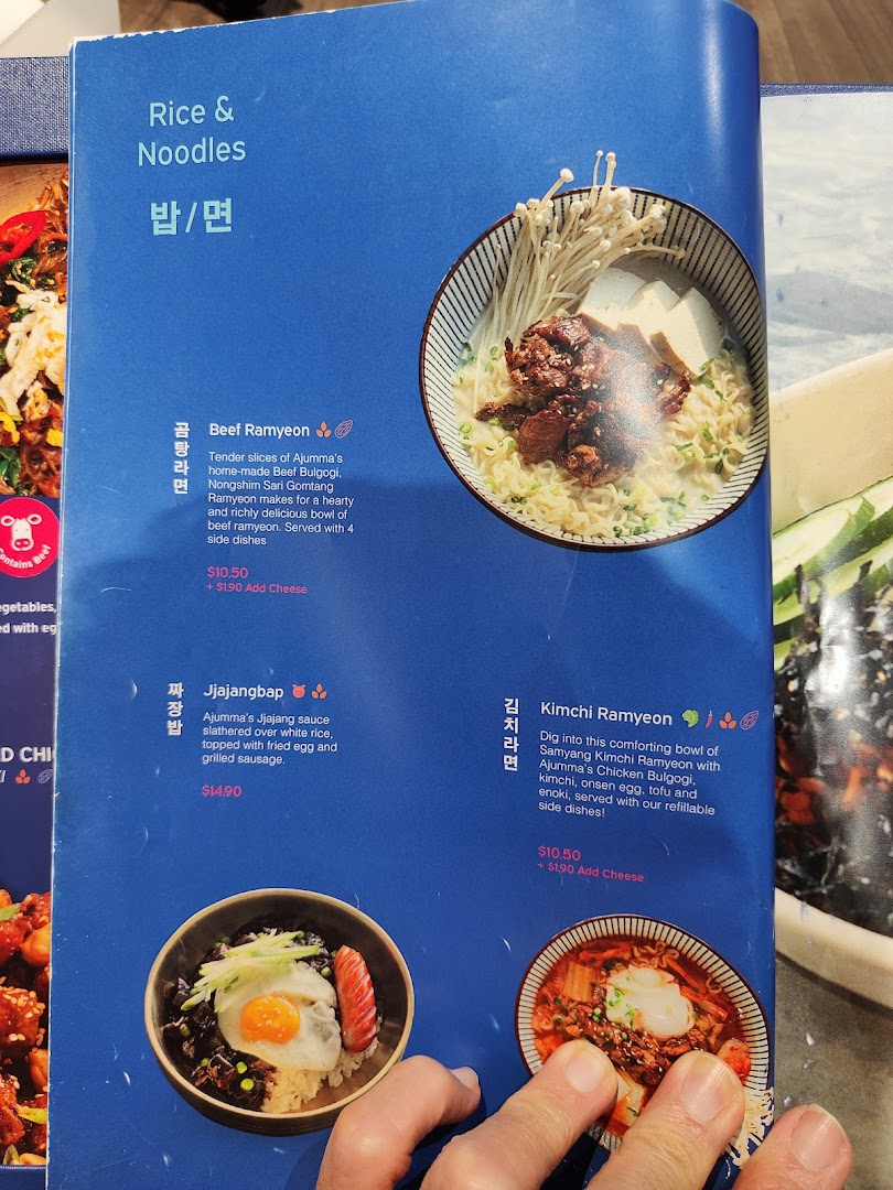 A close-up of Ajummas' menu page featuring Korean rice and noodle dishes with descriptions and prices.