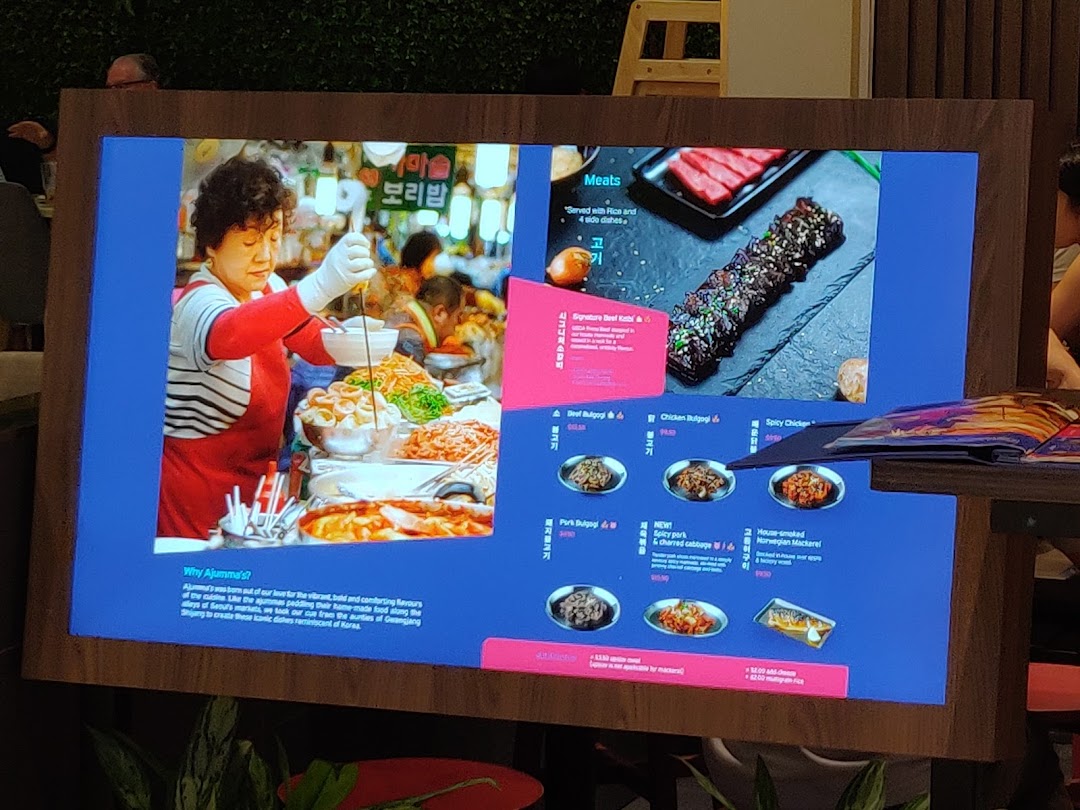 A digital menu board for Ajummas, showcasing Korean dishes with vibrant imagery and descriptions.