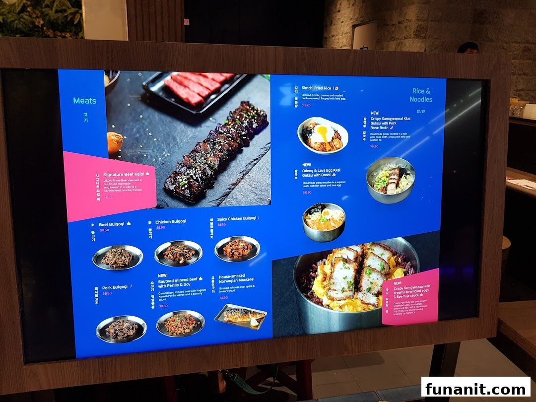A digital menu board at Ajummas displaying various Korean dishes and their prices.
