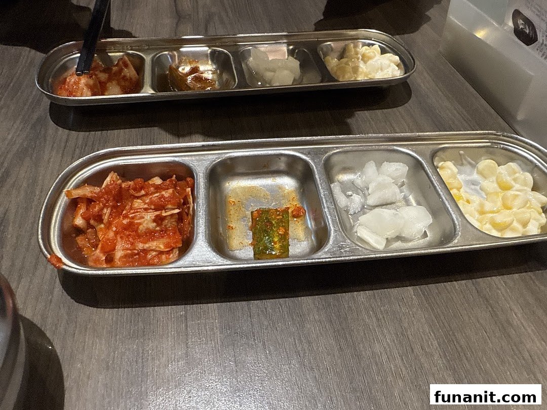 Two metal trays filled with various Korean banchan, including kimchi and corn salad, on a wooden table.