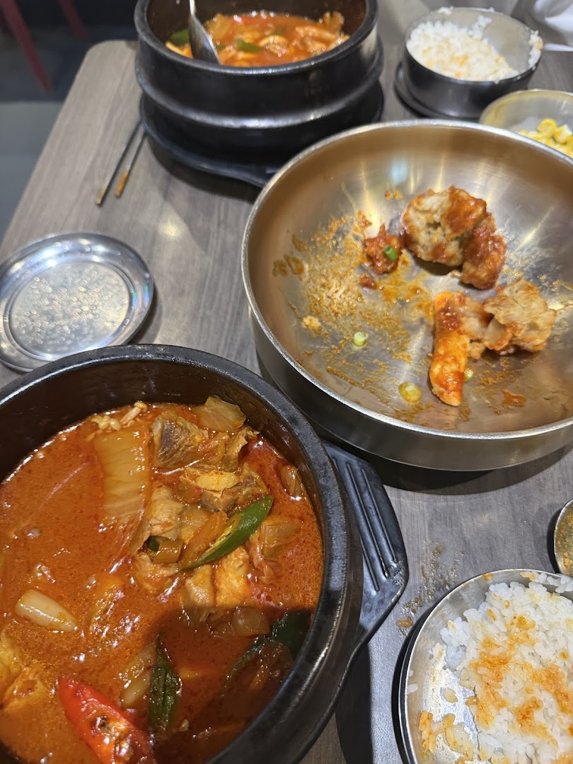 A close-up of various Korean dishes, including a spicy stew and fried items, served on a wooden table.