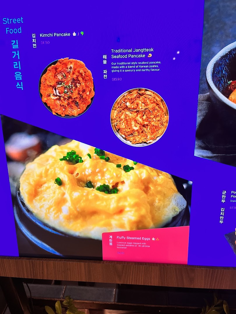 Digital menu board displaying Korean street food items like pancakes and steamed eggs with prices.