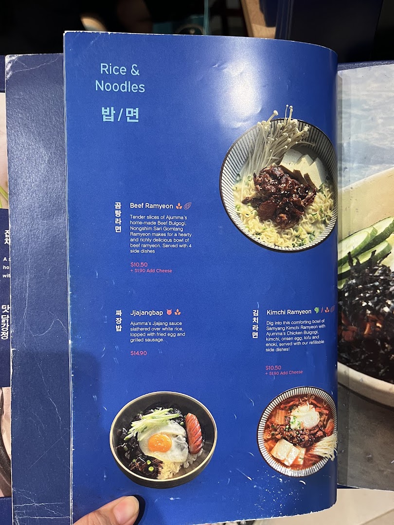 A vibrant blue menu page from Ajummas featuring Korean rice and noodle dishes.