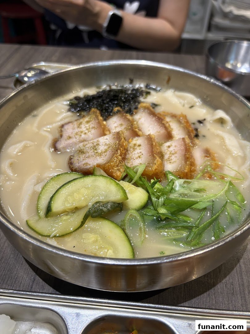 A close-up of a delicious bowl of Korean noodles with crispy pork belly, vegetables, and seaweed.