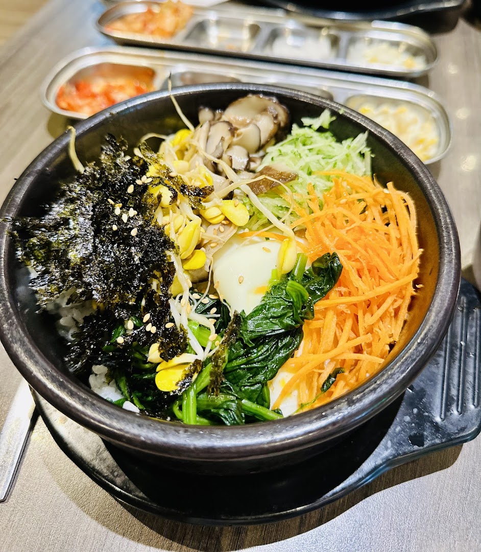 A vibrant bowl of Korean Bibimbap with various fresh vegetables, egg, and seaweed, served with banchan.
