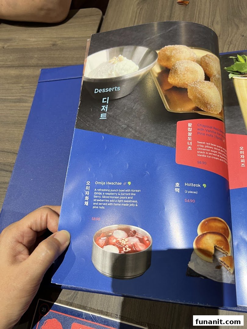 A hand holds open a menu page displaying Korean desserts with descriptions and prices.