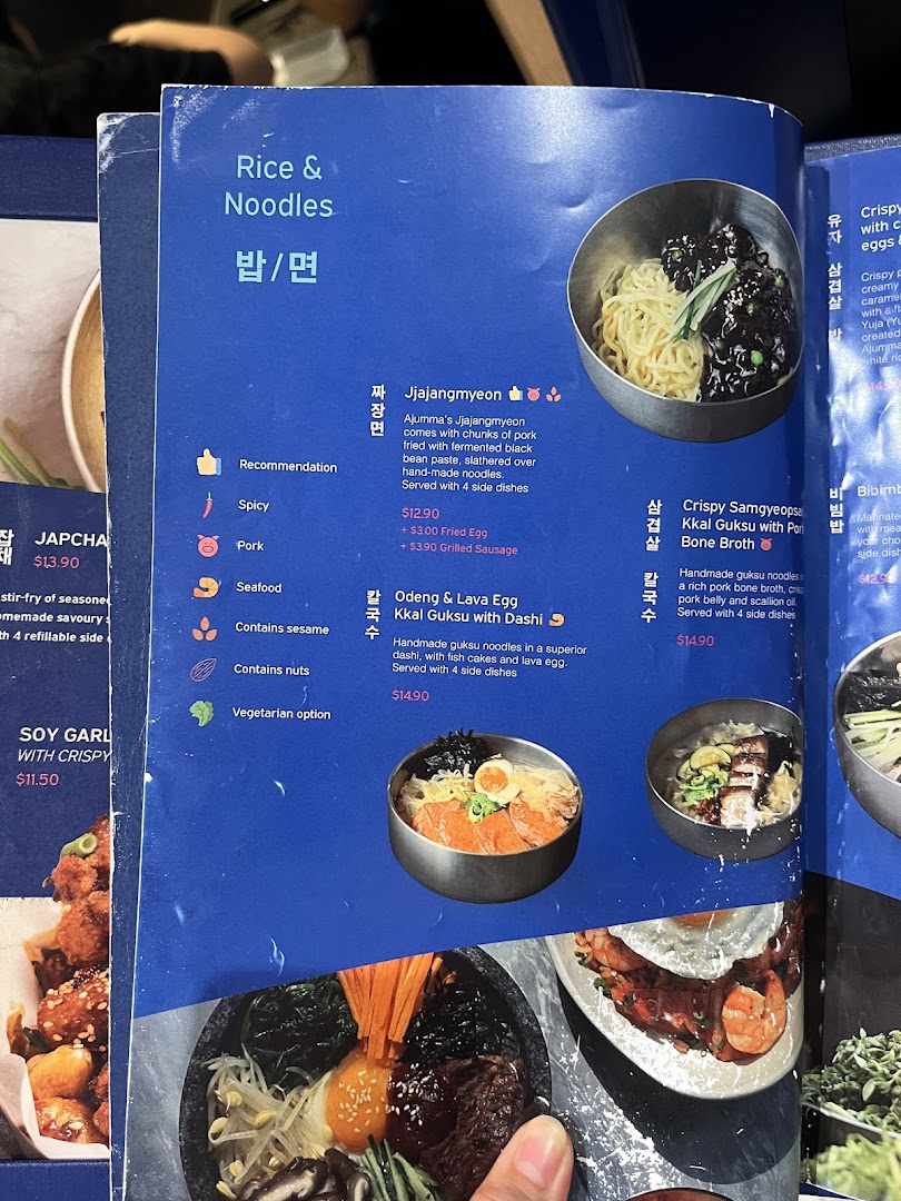 A close-up view of a menu page from Ajummas, featuring rice and noodle dishes.