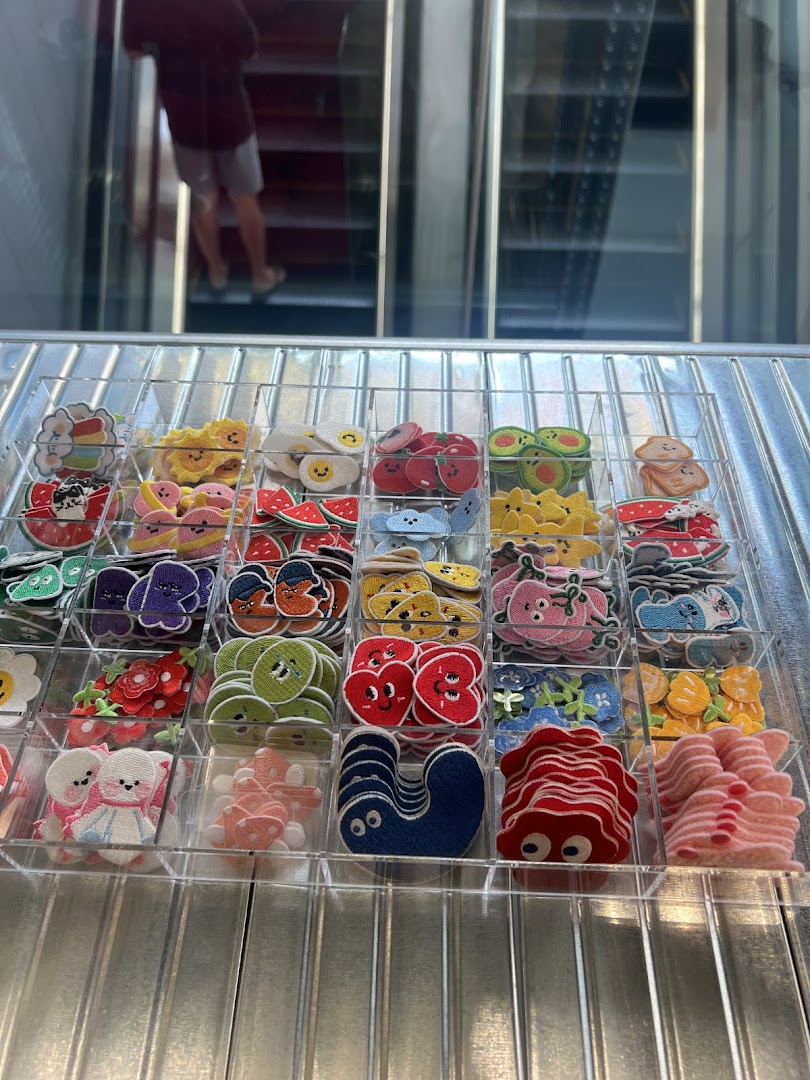 A display of colorful, cartoon-like embroidered patches or pins in clear trays, with an escalator in the background.
