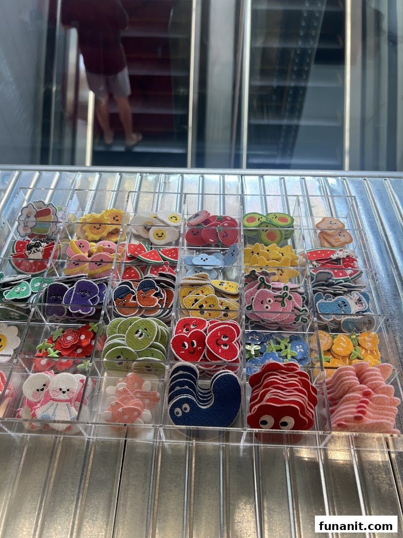 A display of colorful, cartoon-like embroidered patches or pins in clear trays, with an escalator in the background.