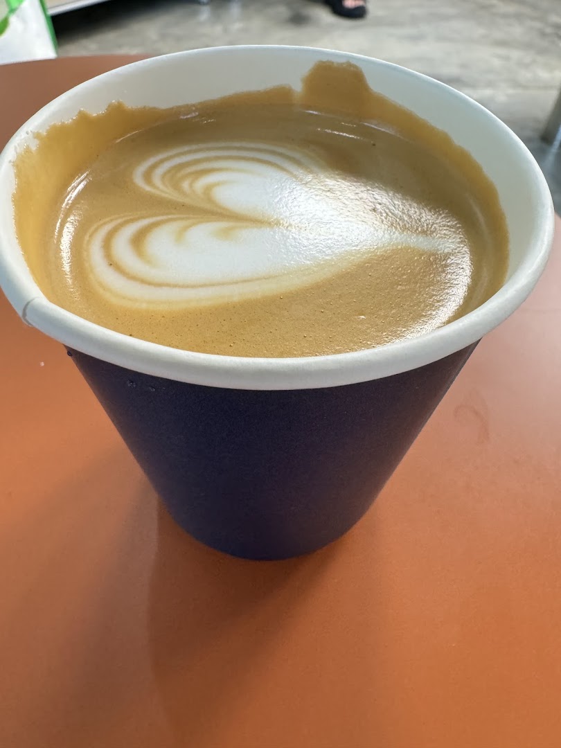 A close-up of a coffee cup with beautiful heart-shaped latte art on an orange table.