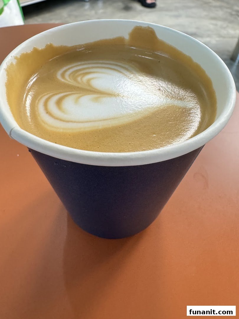 A close-up of a coffee cup with beautiful heart-shaped latte art on an orange table.