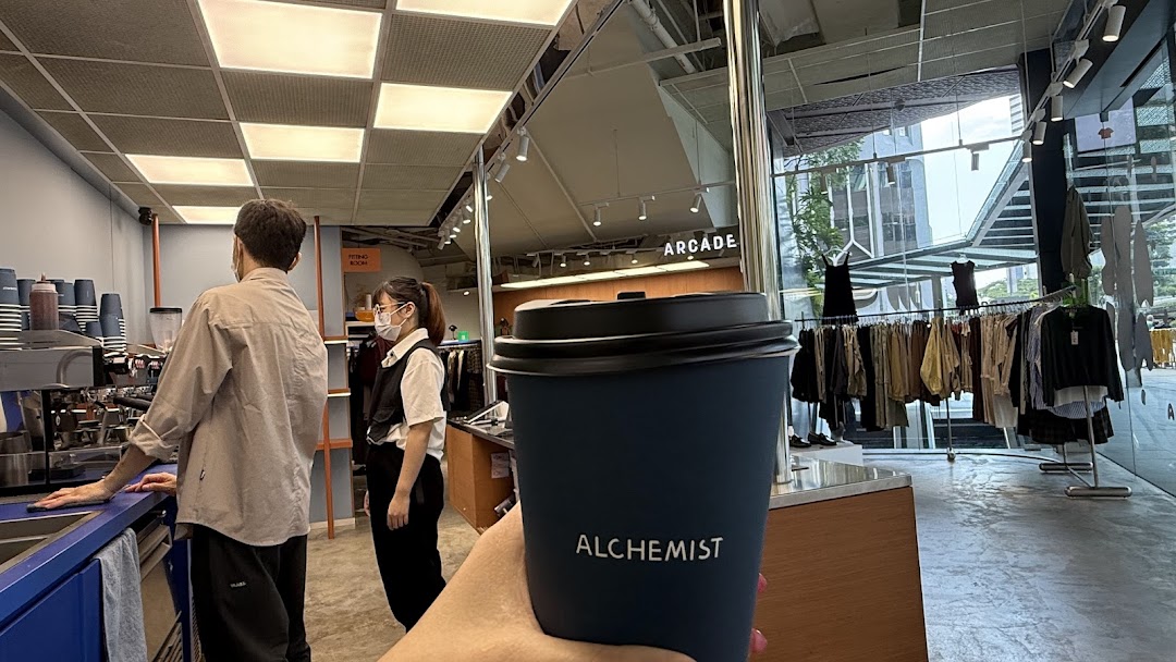 A person holds an Alchemist coffee cup inside a modern shop combining a cafe and clothing retail.