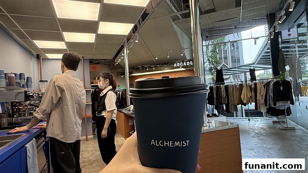 A person holds an Alchemist coffee cup inside a modern shop combining a cafe and clothing retail.