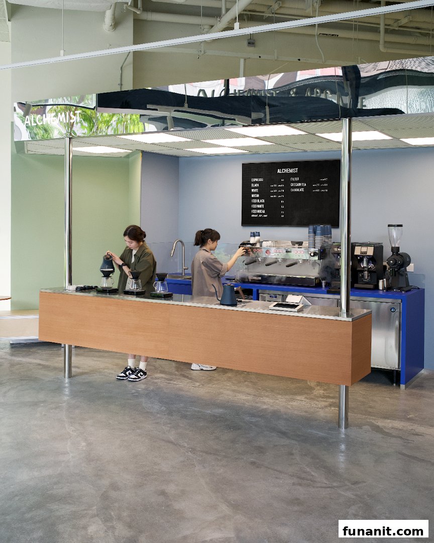 Two baristas preparing coffee at a modern, minimalist coffee bar with a menu board.