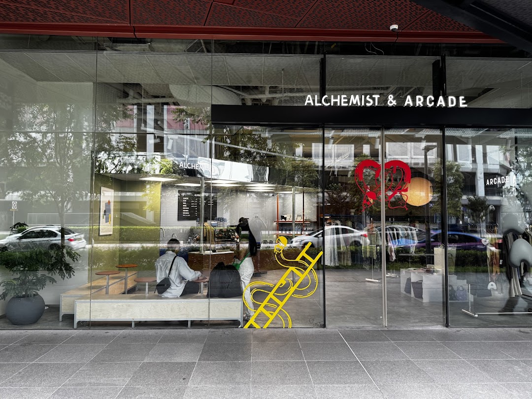 Exterior view of Alchemist & Arcade, showcasing its modern glass facade and inviting interior with a cafe and retail space.