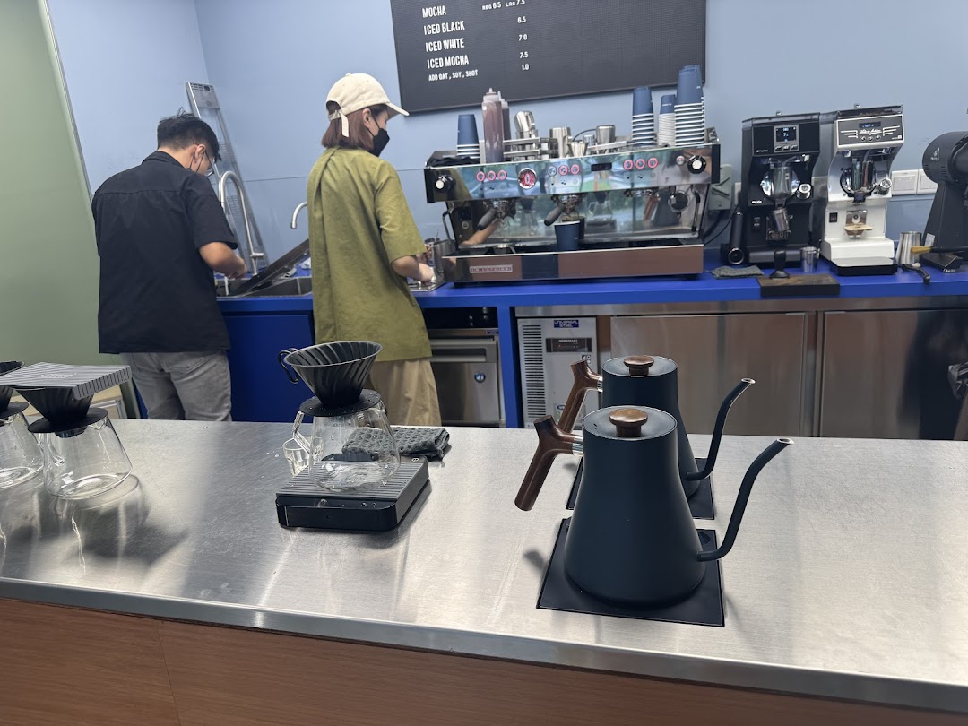 Baristas prepare coffee at a modern counter with brewing equipment and a partial menu board.