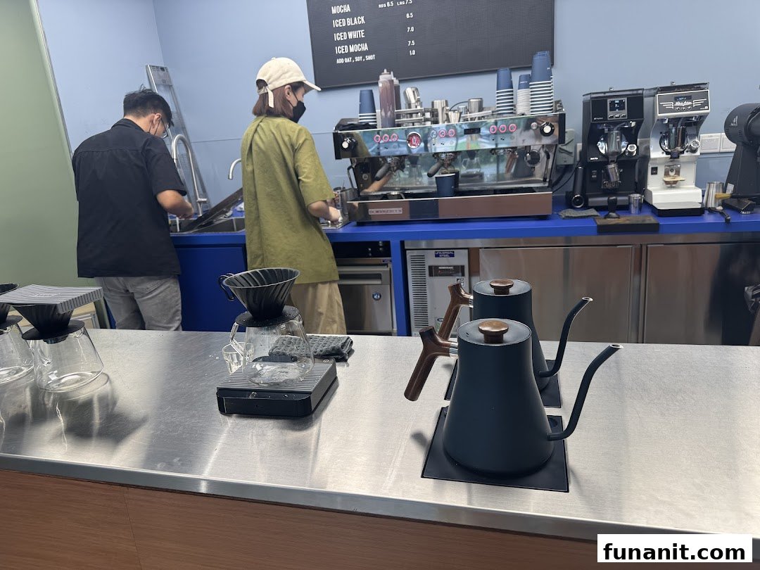 Baristas prepare coffee at a modern counter with brewing equipment and a partial menu board.