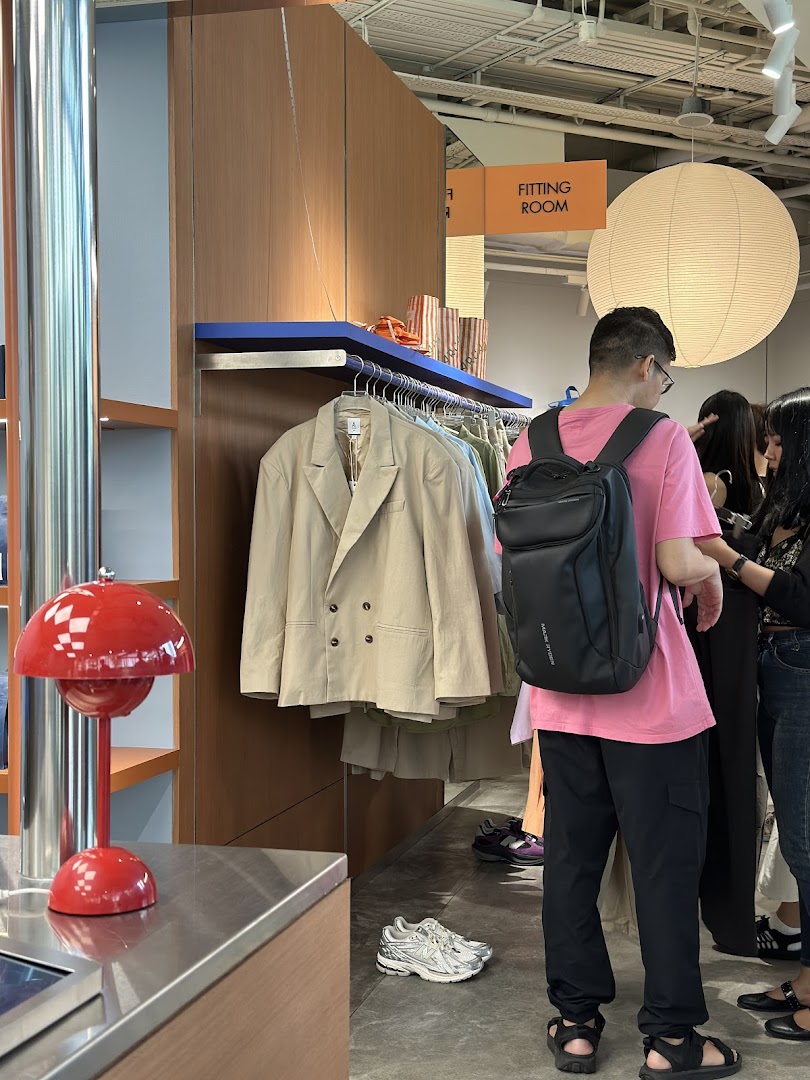 Customers browse clothing racks in a modern retail space with a fitting room sign and stylish decor.