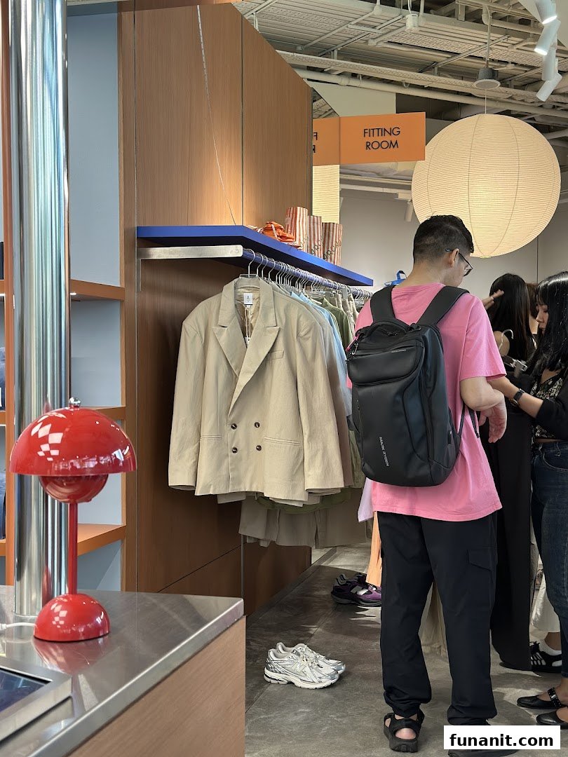 Customers browse clothing racks in a modern retail space with a fitting room sign and stylish decor.