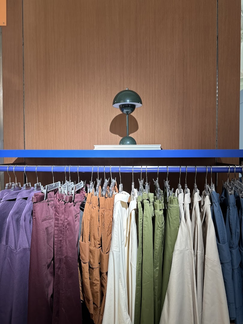 A clothing rack displaying various colored garments with a decorative lamp on a shelf above.