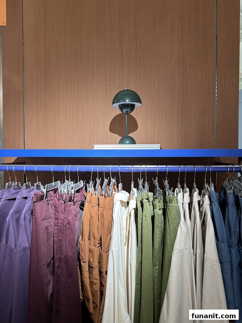A clothing rack displaying various colored garments with a decorative lamp on a shelf above.