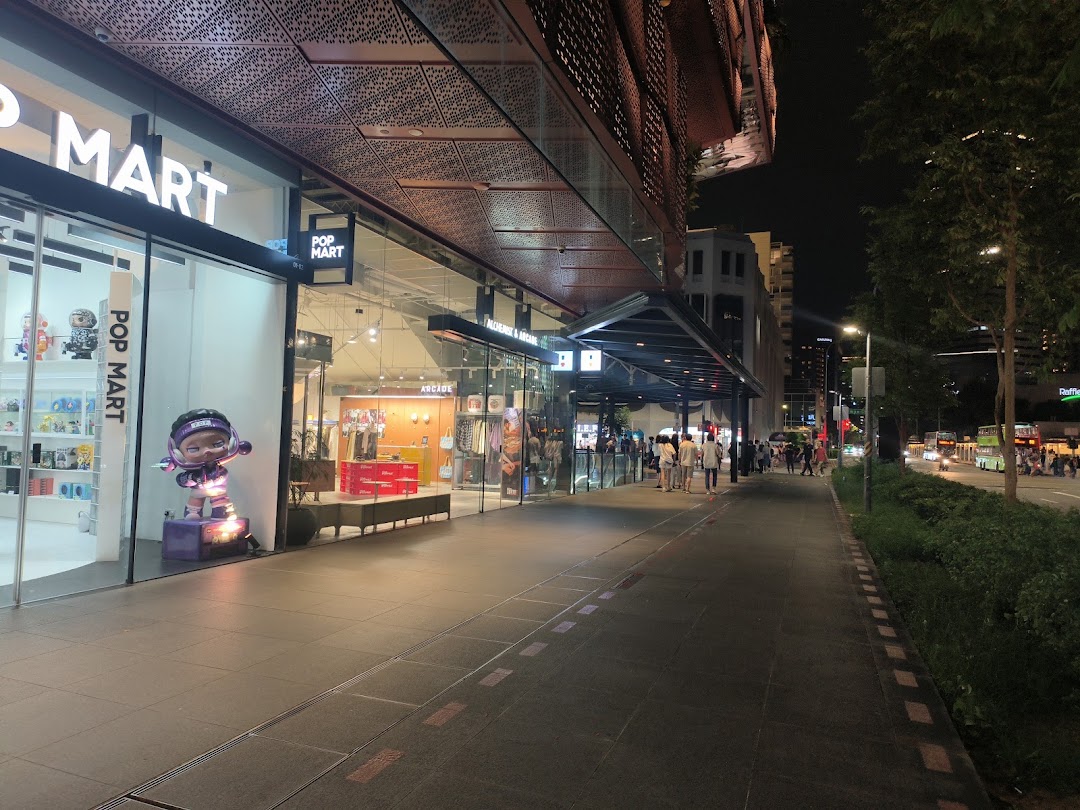 Illuminated storefronts of POP MART and Alchemist x Arcade at night, showcasing unique retail experiences along a bustling sidewalk.