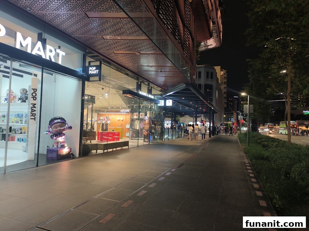 Illuminated storefronts of POP MART and Alchemist x Arcade at night, showcasing unique retail experiences along a bustling sidewalk.