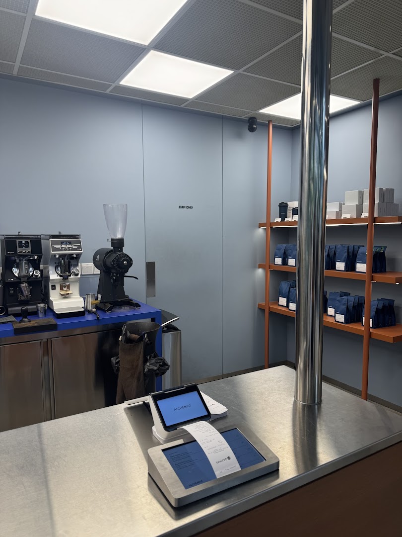 A modern coffee counter with brewing equipment and retail coffee bags on display shelves.