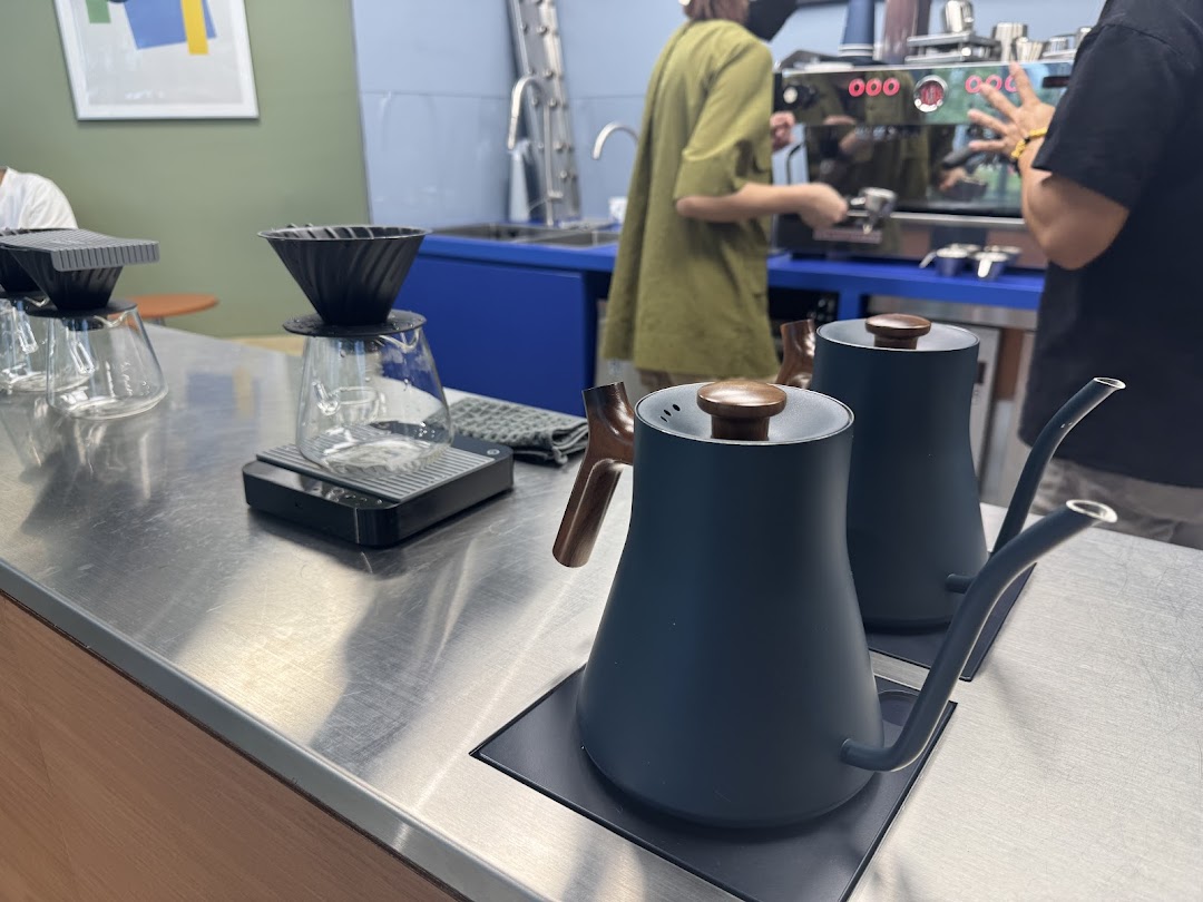 Coffee brewing equipment on a counter with baristas preparing drinks in the background.