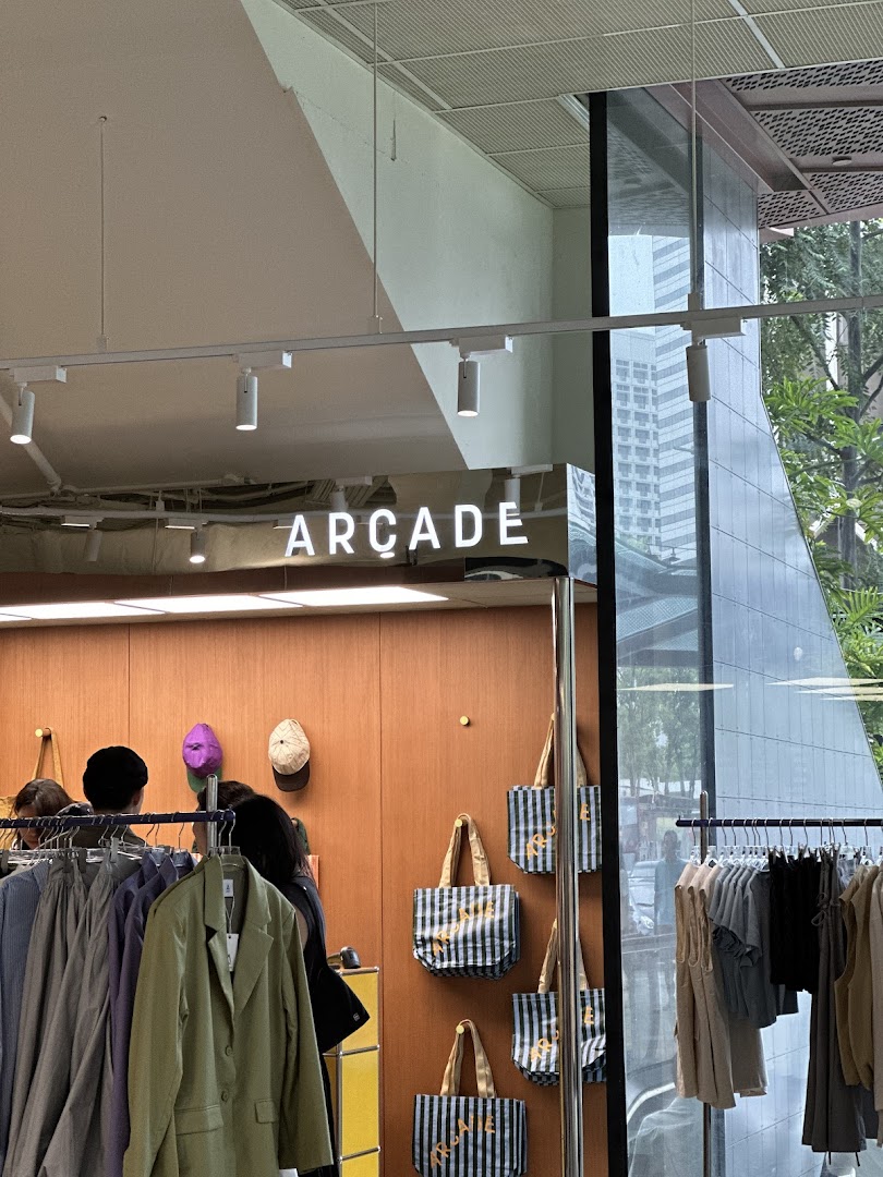 Interior view of 'ARCADE' retail shop, showcasing clothing racks, tote bags, and customers.