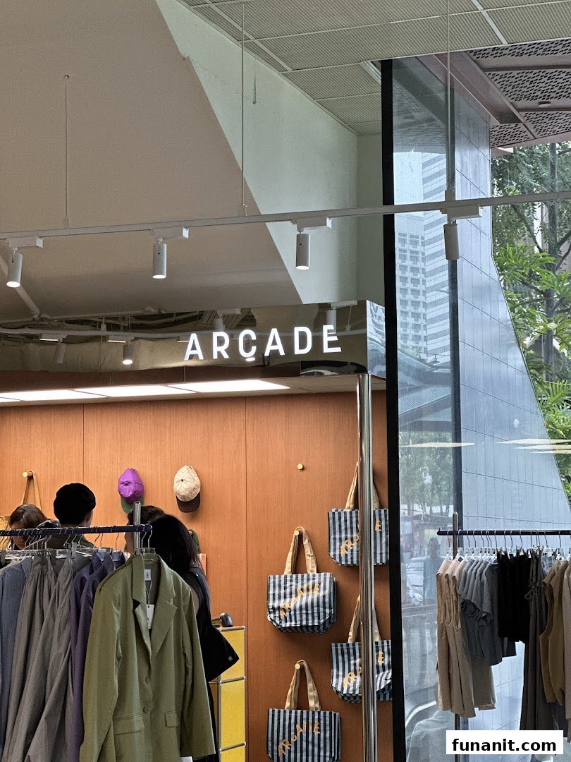 Interior view of 'ARCADE' retail shop, showcasing clothing racks, tote bags, and customers.