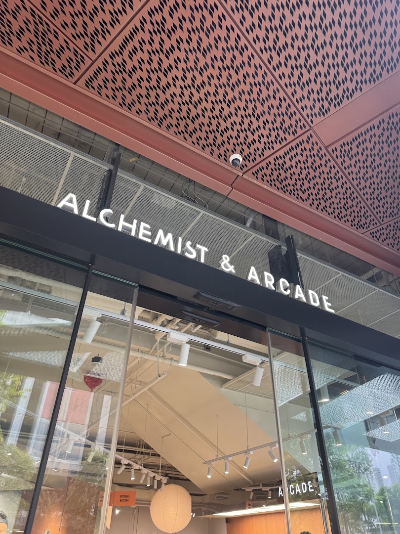 The shop front of Alchemist & Arcade, featuring its prominent illuminated signage and glass entrance.