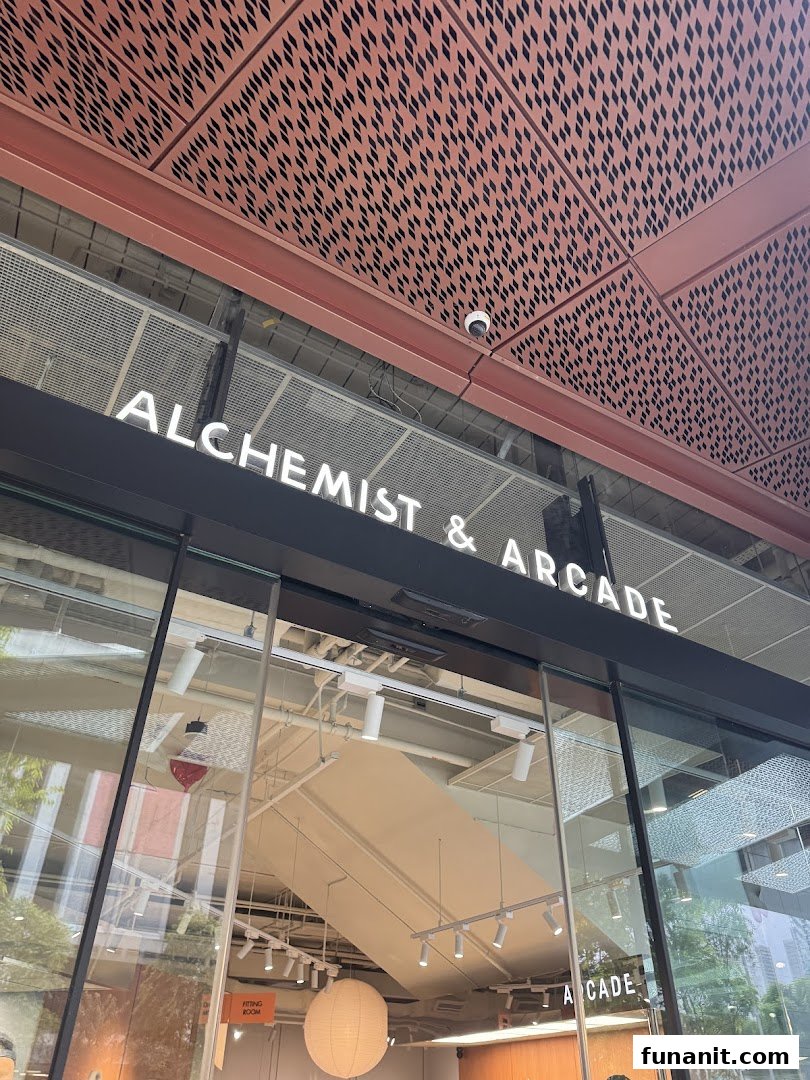 The shop front of Alchemist & Arcade, featuring its prominent illuminated signage and glass entrance.