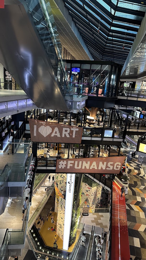 A vibrant multi-level interior view of Funan mall, showcasing escalators, shops, and a climbing wall.