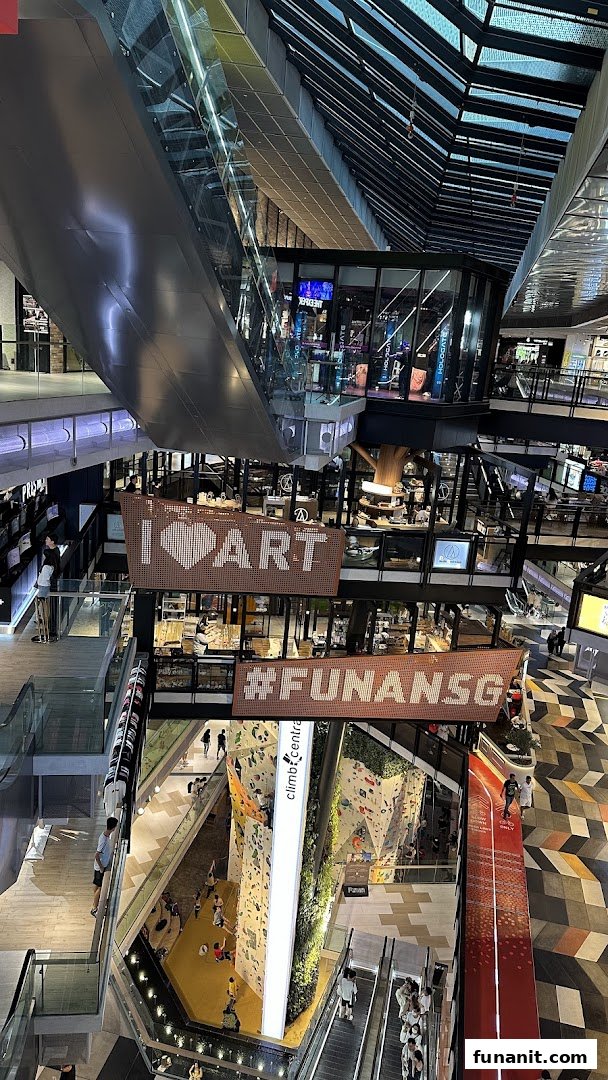 A vibrant multi-level interior view of Funan mall, showcasing escalators, shops, and a climbing wall.
