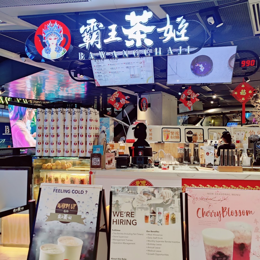 An interior view of a bustling tea shop counter, featuring staff, promotional displays, and branding.