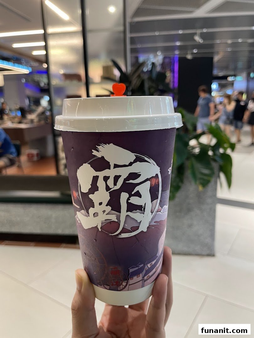 A hand holds a purple beverage cup with Chinese characters, featuring a small red heart on the lid.