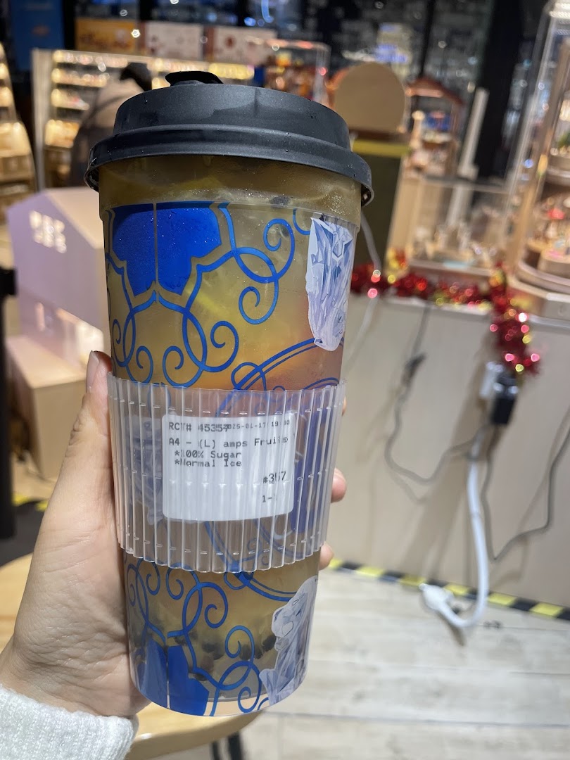 A hand holds a large, refreshing fruit tea drink from Amps Tea, featuring a custom label.