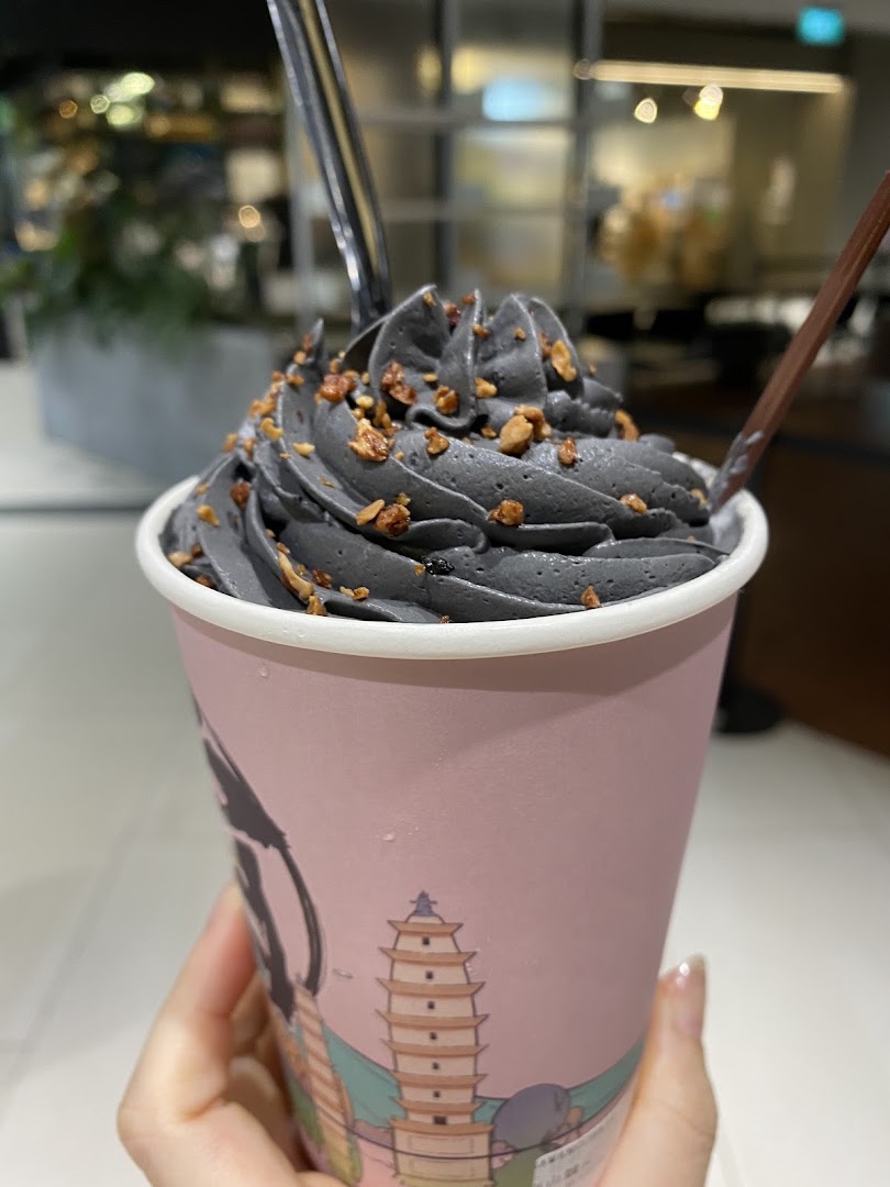 A hand holds a pink cup with dark grey soft serve topped with nuts, likely from amps tea Funan.