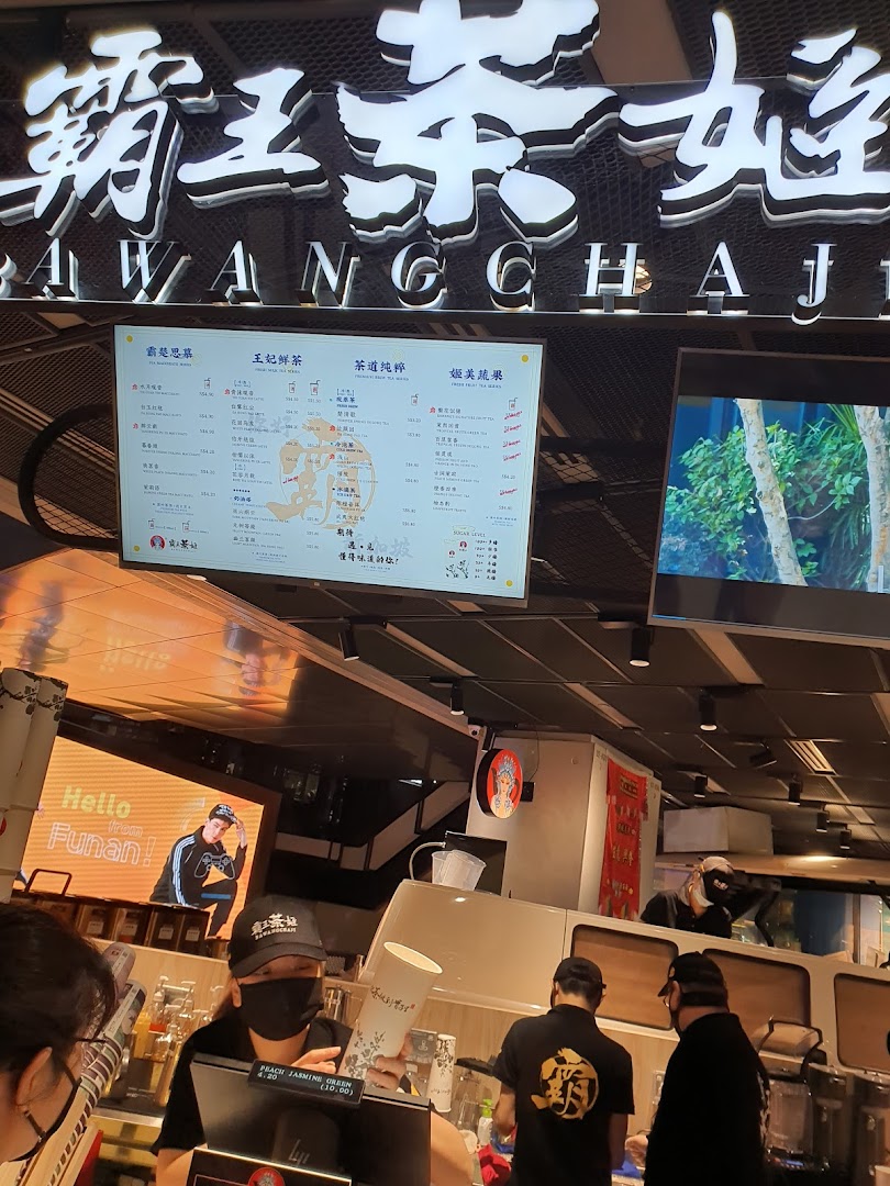 Interior view of a tea shop with a prominent digital menu board and staff at the counter.