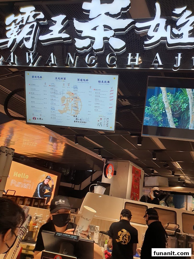 Interior view of a tea shop with a prominent digital menu board and staff at the counter.