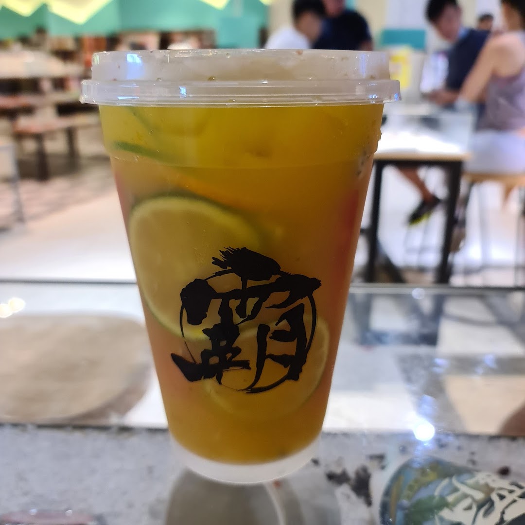 A refreshing fruit tea drink with citrus slices, featuring the shop's logo, in a bustling mall setting.