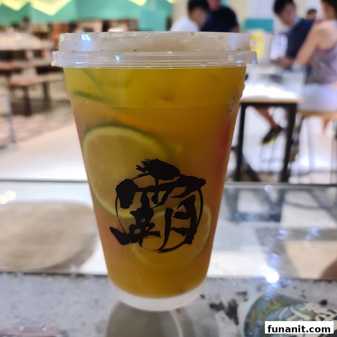 A refreshing fruit tea drink with citrus slices, featuring the shop's logo, in a bustling mall setting.