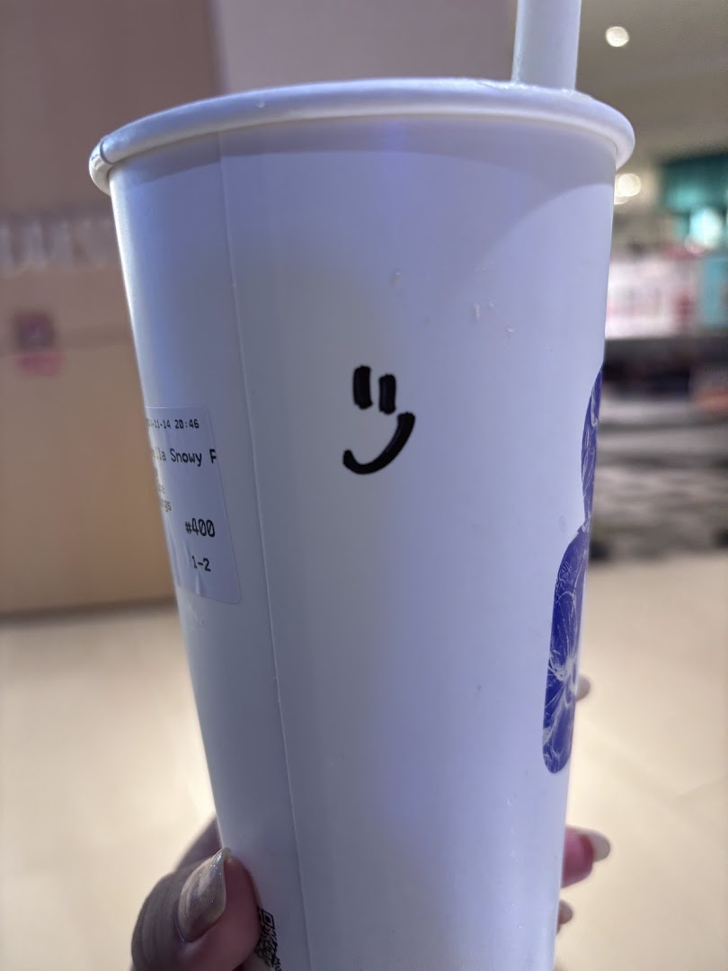 A hand holds a white drink cup from Amps Tea with a smiley face drawn on it.