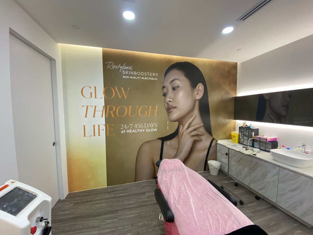 An aesthetic clinic treatment room featuring a large 'Glow Through Life' mural and medical equipment.