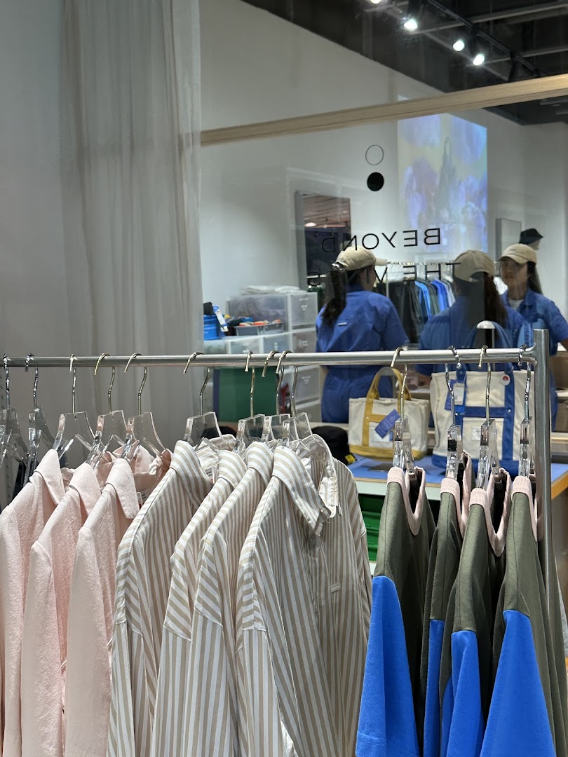A retail display featuring various clothing items on hangers, with the shop's interior and reflection visible.