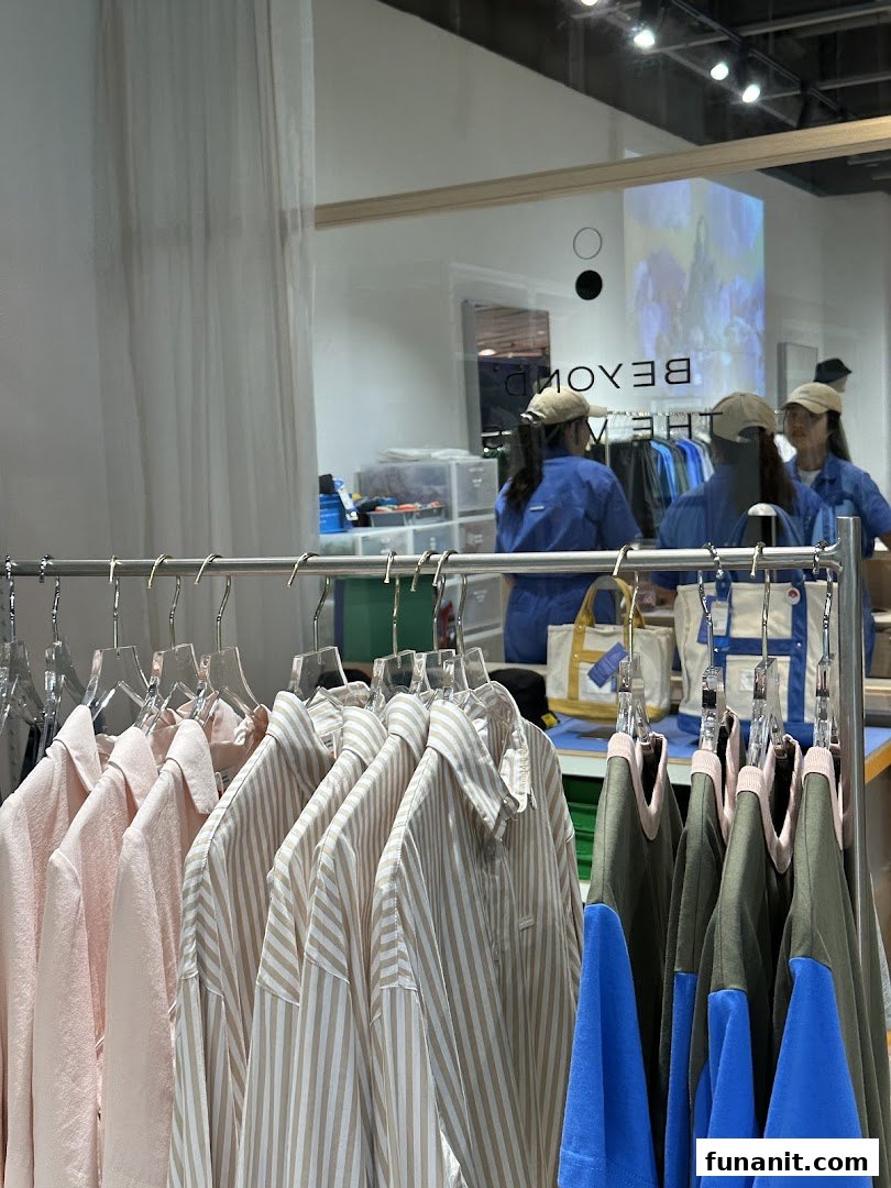 A retail display featuring various clothing items on hangers, with the shop's interior and reflection visible.